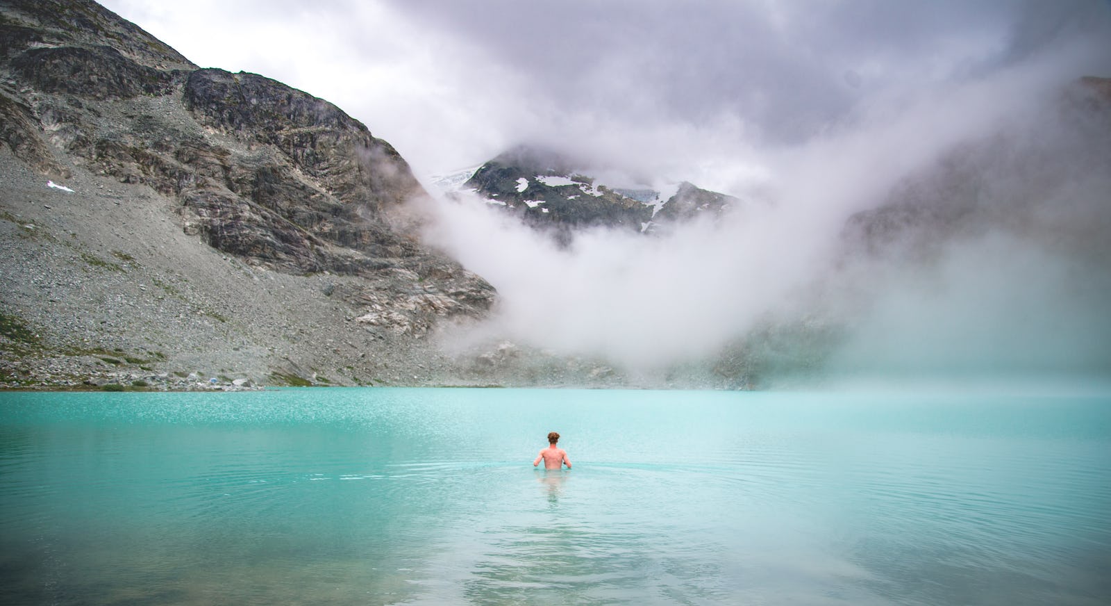 Mann schwimmt in einem Gebirgssee bei Nebel