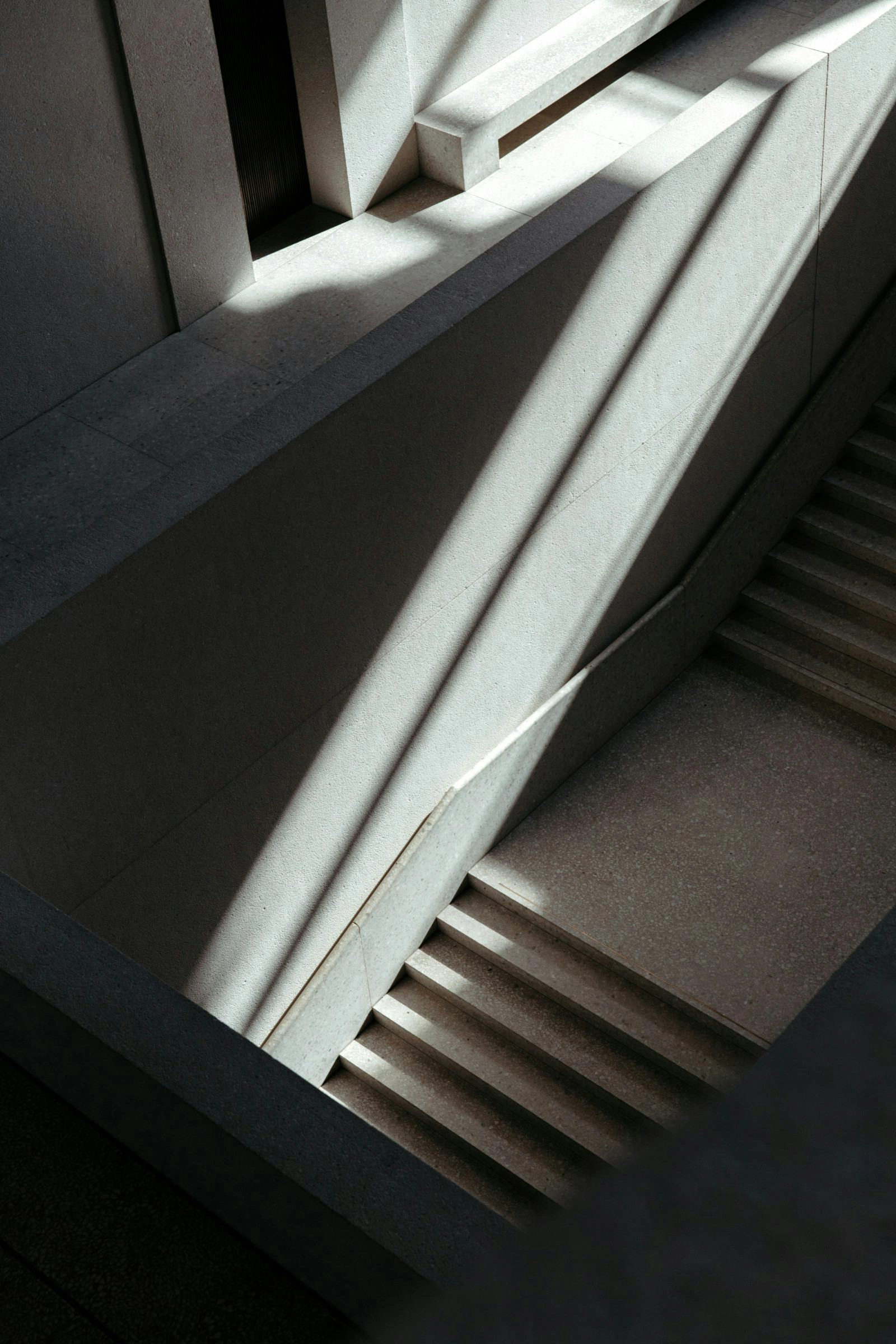 Eine moderne Treppe aus Beton, die von Sonnenlicht beleuchtet wird und scharfe Schatten wirft.