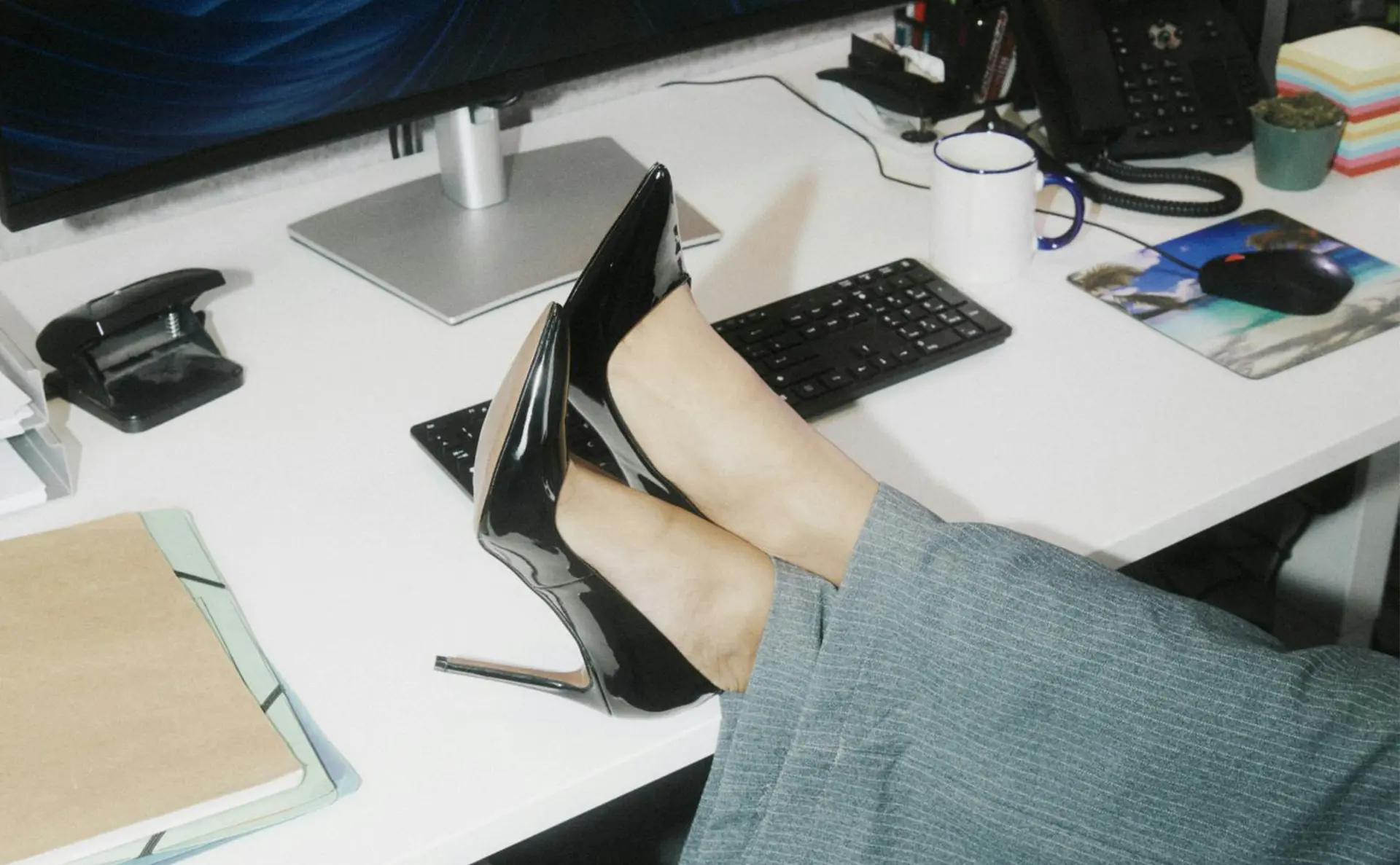 Business Frau mit High Heels hat die Füße am Tisch. Eine Tastatur und ein Computer sind im Hintergrund zu sehen.
