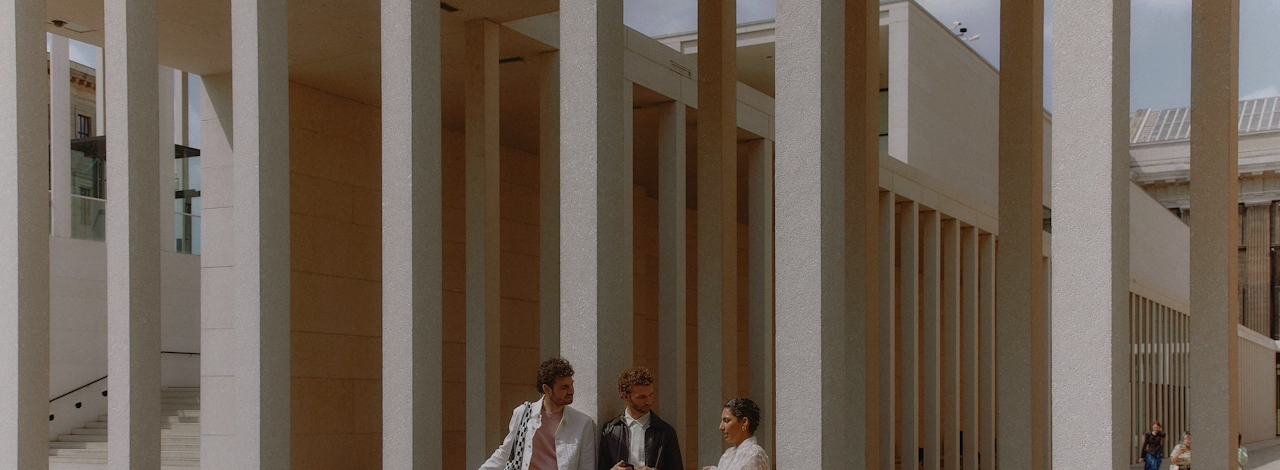 Two men and a woman in front of a light-coloured building