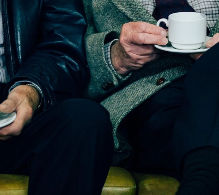 Two elderly men in suits drinking coffee.