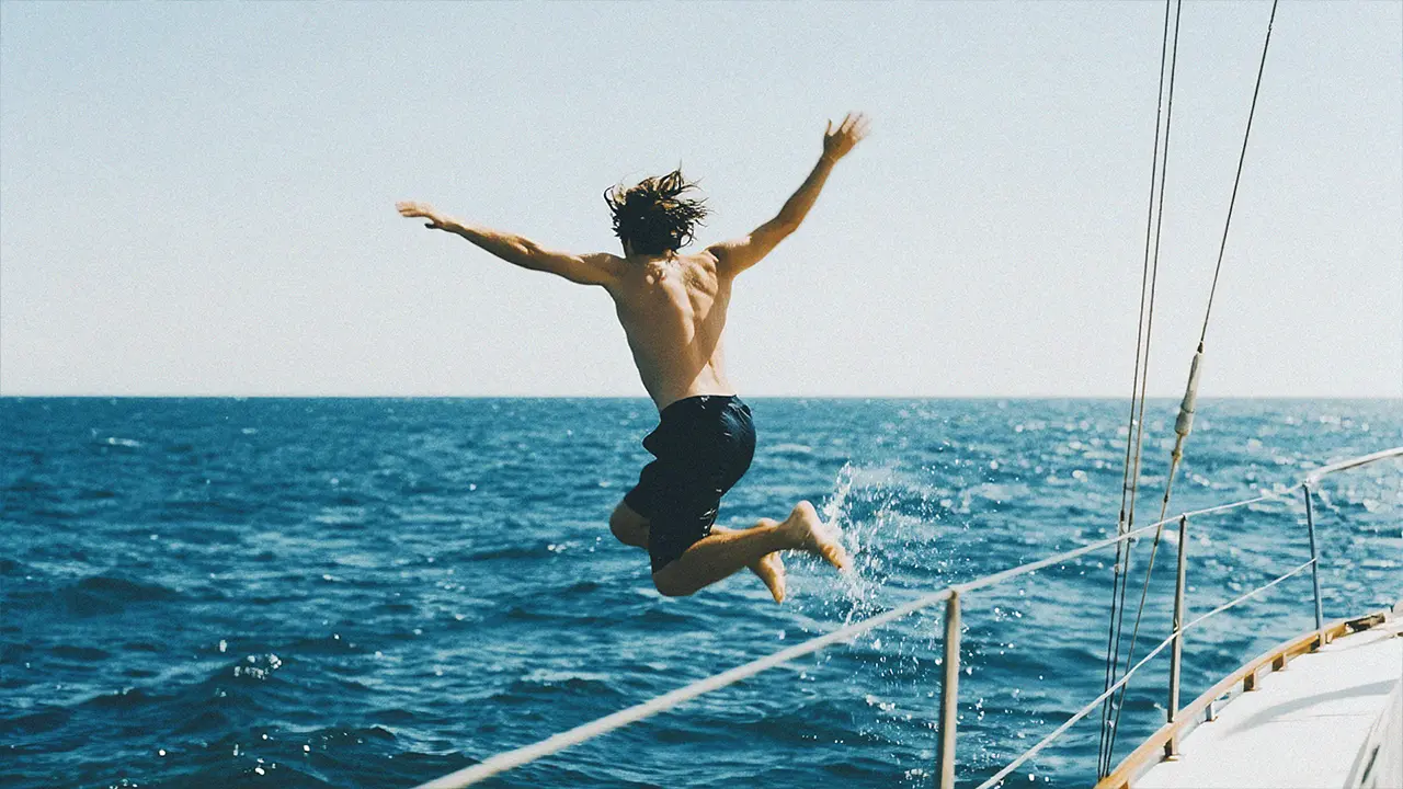 A person diving headfirst into a body of water from a wooden dock. The dock has ropes tied to posts, and the water appears calm.